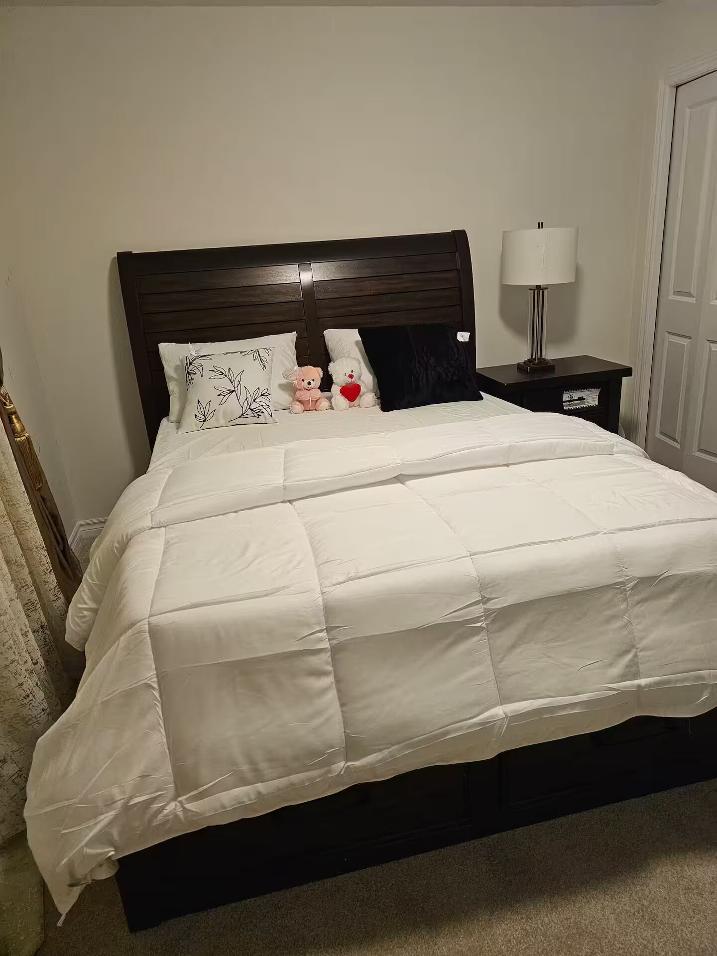 A neatly made bed with a white comforter and pillows, a bedside lamp, and a small nightstand.