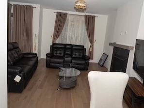 A living room with a fireplace, leather sofas, a glass coffee table, and a TV.