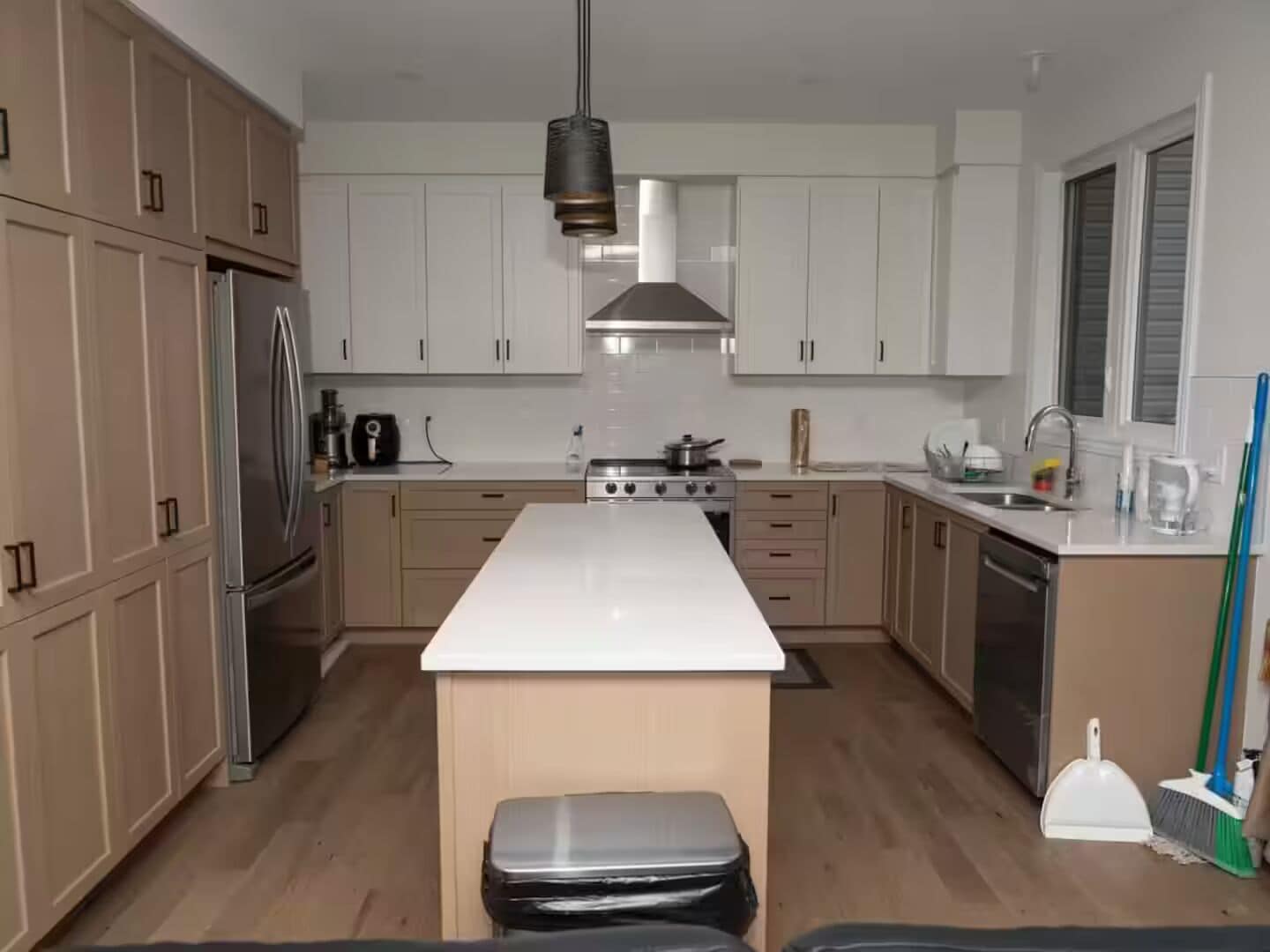 A modern kitchen with white cabinets, a stainless steel refrigerator, a central island, and a hanging light fixture.