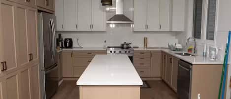 A modern kitchen with white cabinets, a stainless steel refrigerator, a central island, and a hanging light fixture.