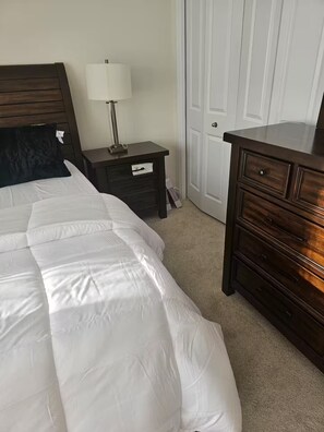 A bedroom with a bed, a nightstand with a lamp, a dresser, and a closet.