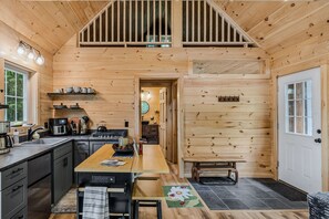A wooden cabin interior with a kitchen, dining area, and a loft bedroom. - Grace Cottage - Serene Private Location (Strafford)