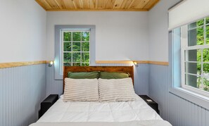 Een slaapkamer met een houten hoofdeinde, een raam met uitzicht op groen, en een nachtkastje.