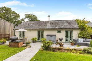 Een huis met een terras, zitplaatsen buiten en een barbecue.