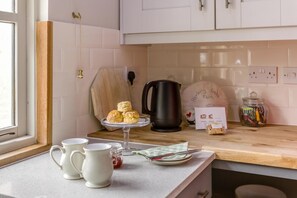A kitchen with a wooden countertop, a coffee maker, a kettle, and a plate with biscuits.