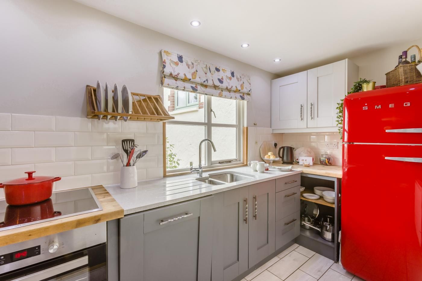A modern kitchen with a red refrigerator, a window with a colorful curtain, and a sink.