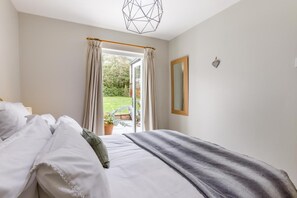 A bedroom with a bed, a window with curtains, a mirror, and a view of the outdoors.