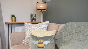 Een gezellige woonkamer met een bank, decoratieve kussens, een vloerlamp, een kleine plant en een radiator.