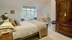 Ein Schlafzimmer mit einem großen Bett, einem Schminktisch mit Spiegeln, einem Holzschrank und einem Fenster mit Blick.