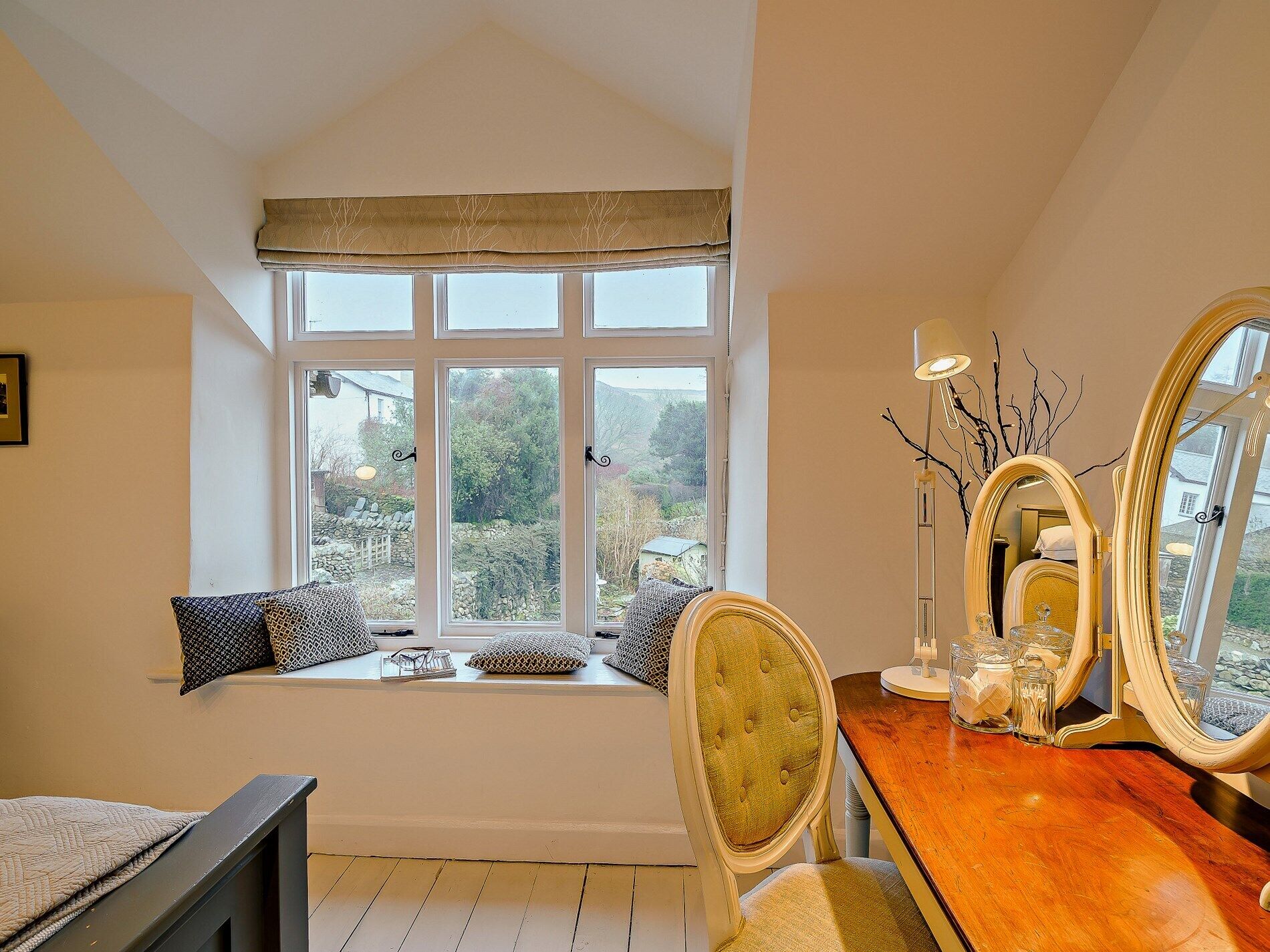 A room with a large window, a wooden vanity with a mirror, and a chair.