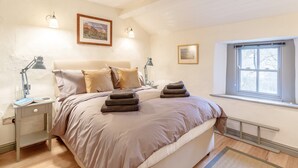 Une chambre à coucher avec un lit, des lampes de chevet, une table de chevet, une fenêtre et deux tableaux encadrés accrochés au mur.