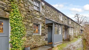 Un bâtiment en pierre recouvert de lierre, un chemin en pierre et une petite porte.