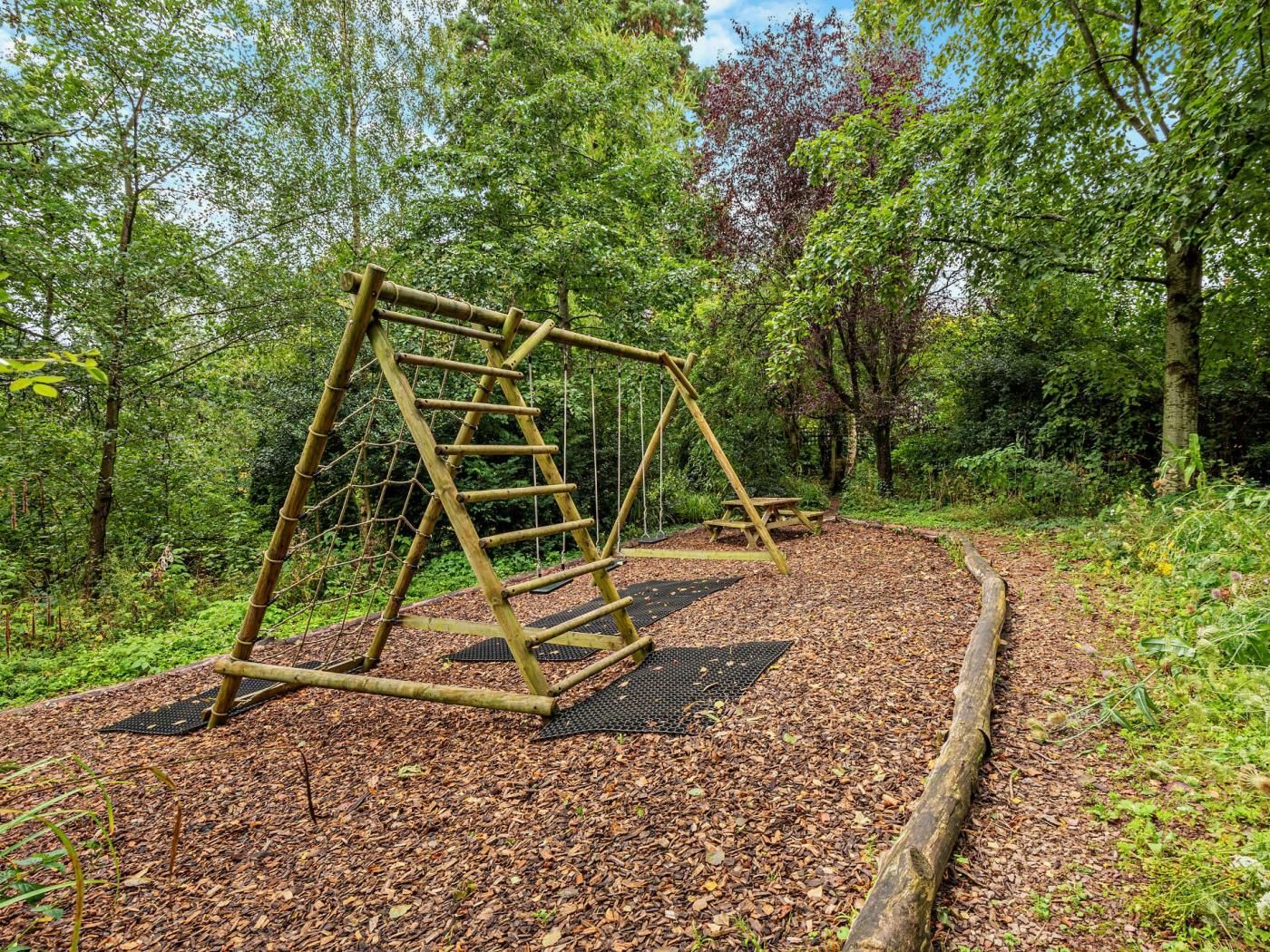 A wooden swing set in a wooded area with a picnic table nearby.
