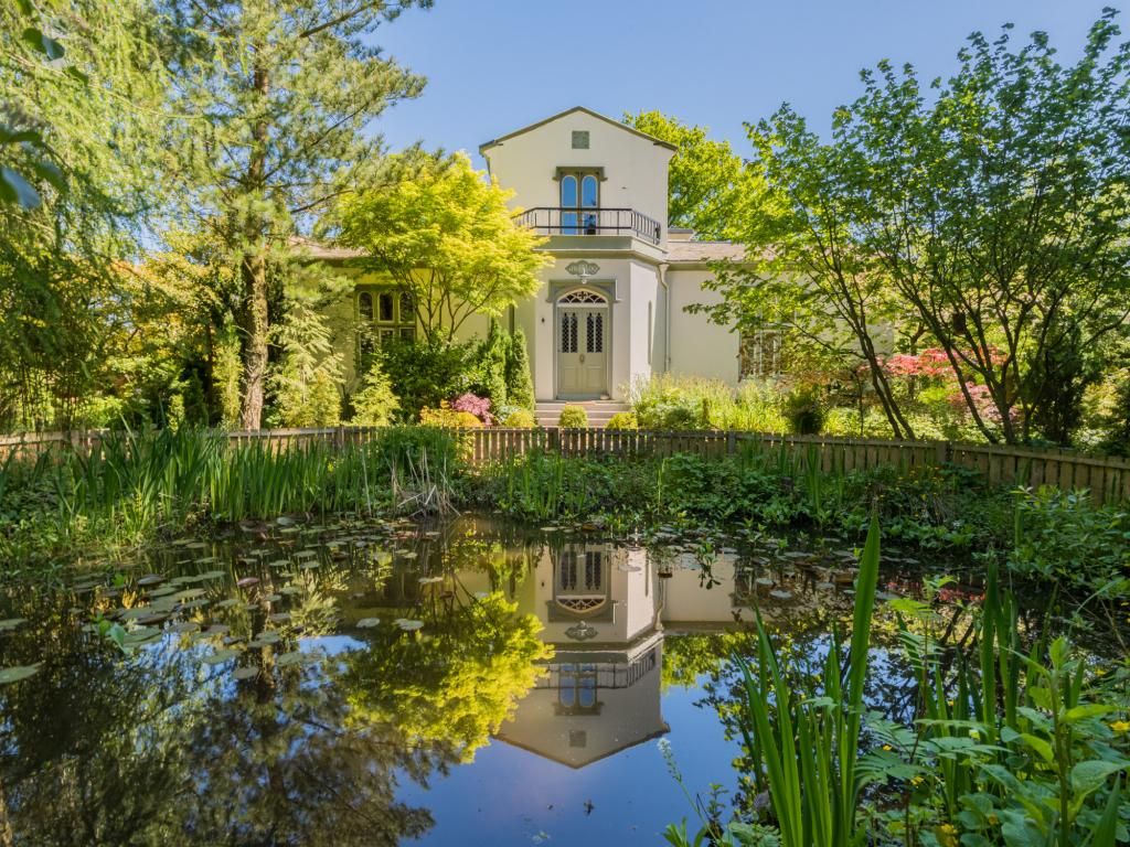 A two-story building with a balcony, surrounded by a pond with lily pads and various plants.