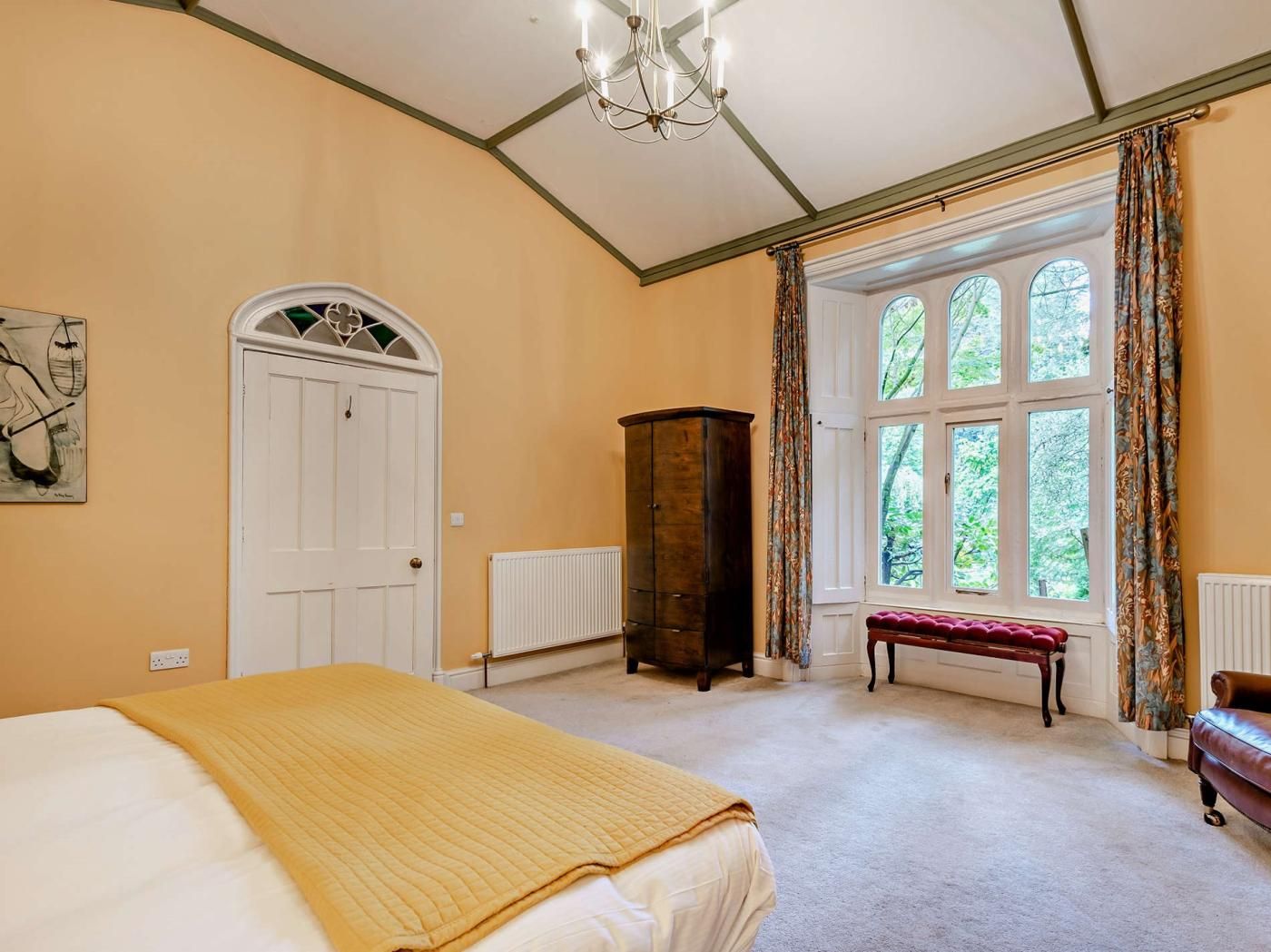 A bedroom with a bed, a radiator, a wooden cabinet, a bench, and a window with curtains.
