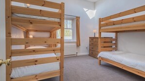 Ein Zimmer mit zwei Etagenbetten, einem Vorhangfenster, einem Heizkörper und einer kleinen Kommode.