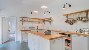 Eine moderne Küche mit weißen Schränken, einer Holz Arbeitsplatte, Pendelleuchten und einem eingebauten Backofen.