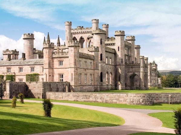 A large castle with multiple towers and arched windows, surrounded by a well-maintained lawn and a curved driveway. - 1 Bed in Penrith (oc-sz003) (Penrith)