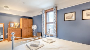 Ein Schlafzimmer mit einem Bett, einem Holzschrank, einem Spiegel, einem Ventilator und einem Fenster mit Vorhängen.
