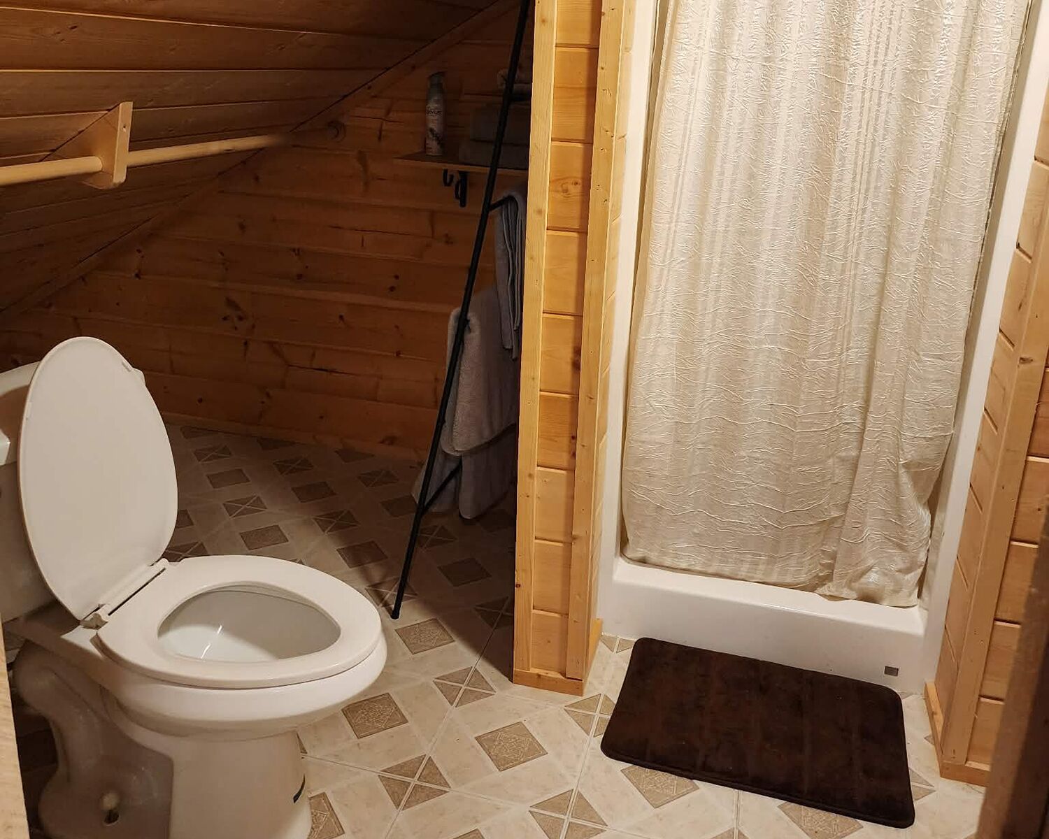 A wooden cabin bathroom with a toilet, shower curtain, and tiled floor.