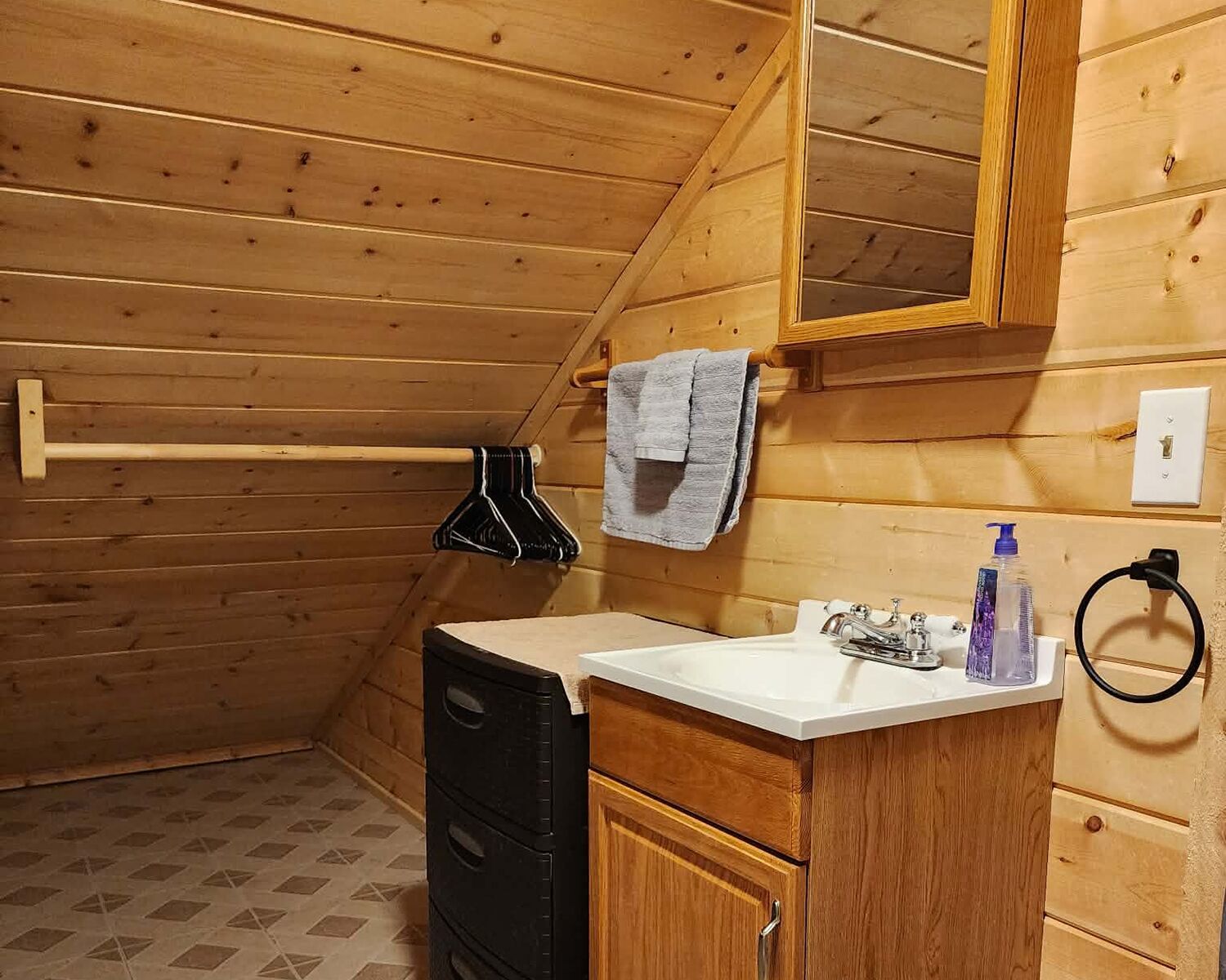 A wooden cabin bathroom with a sink, mirror, towel rack, and a black appliance.