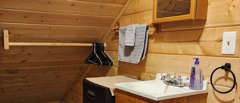 A wooden cabin bathroom with a sink, mirror, towel rack, and a black appliance.
