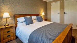 A neatly made bed with a patterned bedspread, two bedside lamps, a wooden nightstand with drawers, and a wardrobe with double doors. - 1 Bed in Outgate and Tarn Hows (78403) (Outgate)