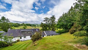 A white building with a sloped roof, surrounded by green grass and trees. - 1 Bed in Outgate and Tarn Hows (78403) (Outgate)