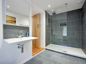 Een moderne badkamer met een glazen douchecabine, een wit wastafelmeubel met houten details en donkere betegelde wanden.