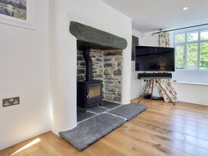A room with a stone fireplace, a flat-screen TV on a stand, and a window with a view of greenery. - 3 Bed in Windermere (oc-sz596) (Windermere)