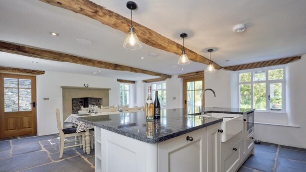 A spacious kitchen with a large island, wooden beams, pendant lighting, and a stone floor. - 3 Bed in Windermere (oc-sz596) (Windermere)