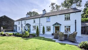 A white building with a garden patio, a dining area with wicker furniture, and a stone wall. - 3 Bed in Windermere (oc-sz596) (Windermere)