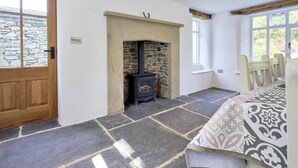 A room with a stone fireplace, a bed with patterned bedding, a wooden door, and a window with a view of greenery. - 3 Bed in Windermere (oc-sz596) (Windermere)