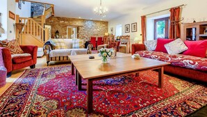 A spacious living room with a wooden coffee table, red and patterned rugs, a stone wall, and a staircase. - 6 Bed in St Bees (SZ558) (Rottington)
