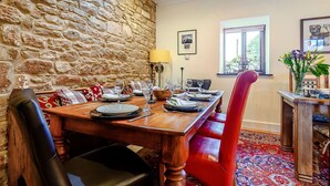 A dining area with a stone wall, a wooden table set for four, and a red chair. - 6 Bed in St Bees (SZ558) (Rottington)