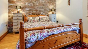 A bedroom with a wooden bed, a stone wall, and two bedside tables with lamps. - 6 Bed in St Bees (SZ558) (Rottington)