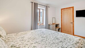 Een slaapkamer met een bed, een kaptafel, een spiegel, een raam met gordijnen en een televisie aan de muur.