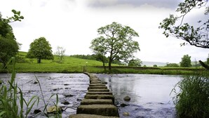 Een stenen brug over een rivier, met grasrijke oevers en bomen op de achtergrond.
