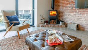A modern living room with a fireplace, a leather sofa, a dining area with chairs, and a balcony with a view. - 2 Bed in Stockport (oc-83789) (Mellor)