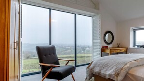 A bedroom with a large window, a chair, a bed, a bedside table, and a mirror. - 2 Bed in Stockport (oc-83789) (Mellor)
