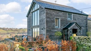A two-story wooden house with a sloped roof, large windows, and a stone wall in the foreground. - 2 Bed in Stockport (oc-83789) (Mellor)