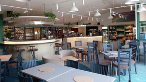 Un caffè moderno con diverse aree salotto, un bar e una varietà di piante.