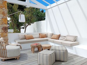 Ein überdachter Außenbereich mit weißer Wand, Steinpfeiler und Blick auf Bäume.