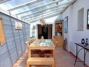 Ein Essbereich mit einem Holztisch und Stühlen, einer Bank, einer Glasdecke und einem Holzschrank mit Dekorationen.