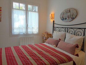 A bedroom with a bed, a window with curtains, a wall-mounted lamp, and a decorative plate. - Moussaillon - Saint Gilles Croix de Vie (SAINT GILLES CROIX DE VIE)