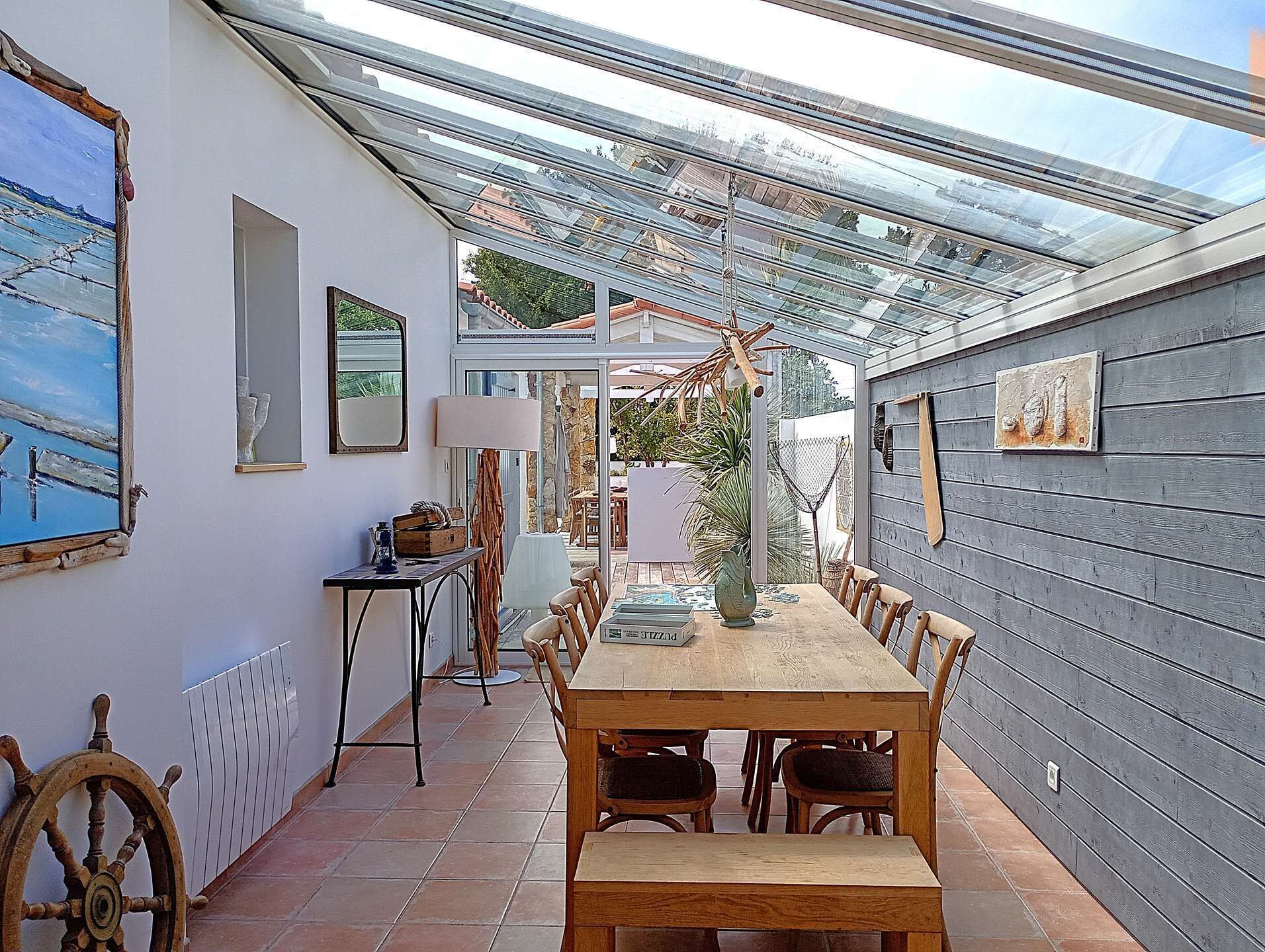 Une terrasse couverte avec une table et des chaises en bois, une lampe et un gouvernail de bateau.
