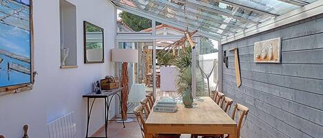 A covered patio with a wooden table and chairs, a lamp, and a ship's wheel.