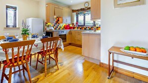 A kitchen with wooden cabinets, a dining table with chairs, a window, and a painting on the wall. - 2 Bed in Appleby-in-westmorland (oc-91029) (Dufton)