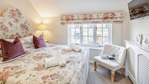 Ein Schlafzimmer mit Bett, Sessel, Schreibtisch, Lampe und einem Fenster mit Blick.