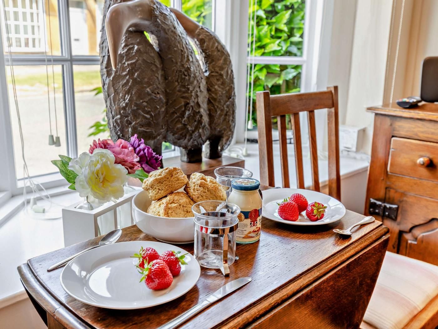 Een eettafel met een bord aardbeien, een schaal scones en een glas water.